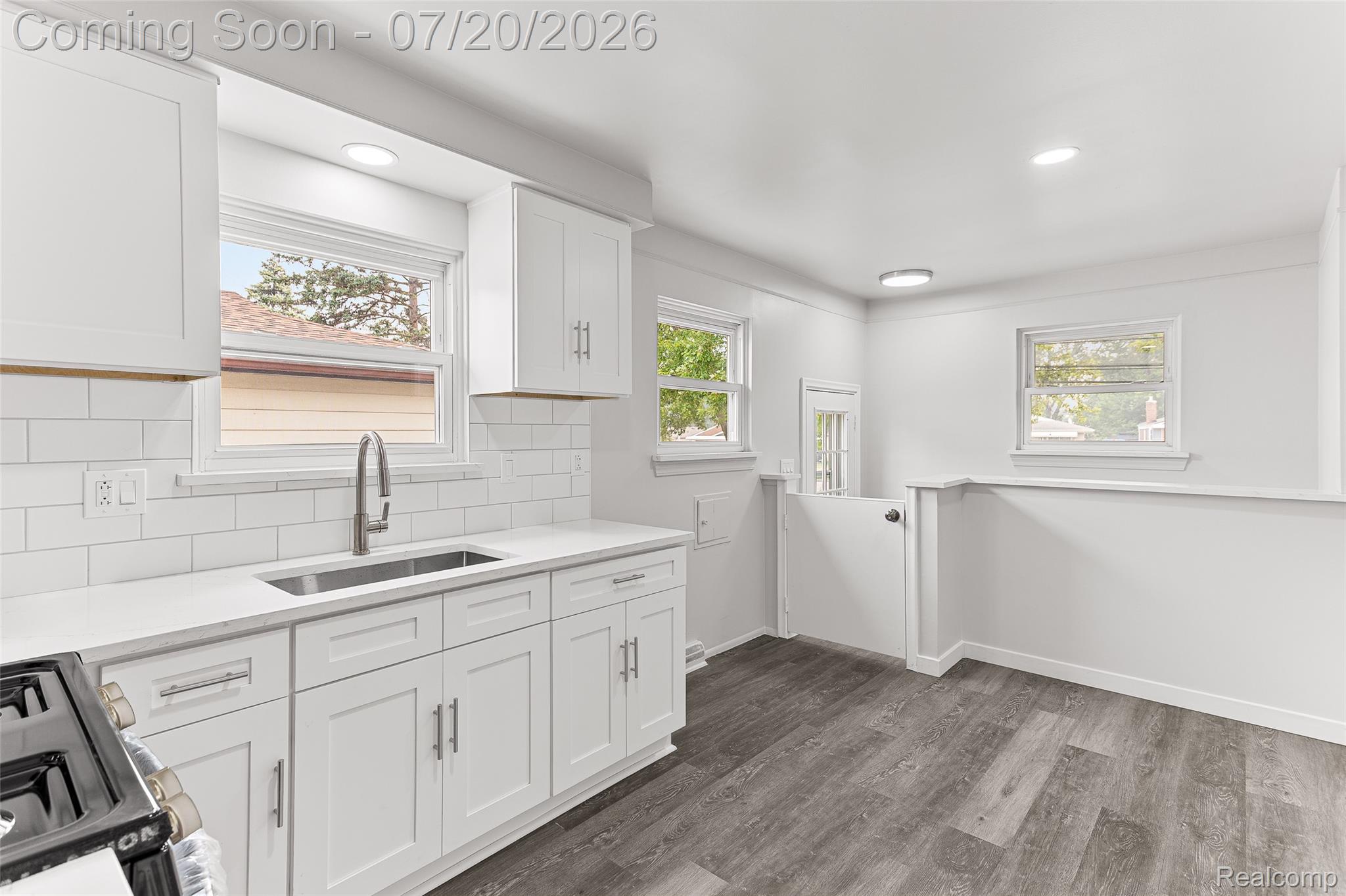 7884 Pardee Road Taylor, MI 48180 - Photo 7 of 23 Bright kitchen featuring white shaker cabinetry, white subway tile backsplash, white countertops, stainless steel undermount sink with gooseneck faucet, and wood-finish flooring