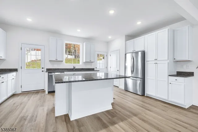 a kitchen with stainless steel appliances granite countertop a refrigerator a sink dishwasher and white cabinets with wooden floor