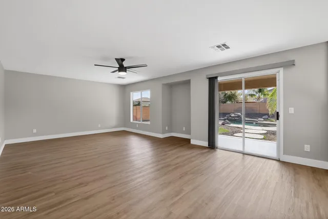 a view of an empty room with wooden floor and a ceiling fan