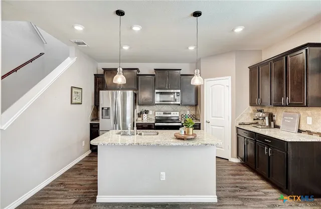 a kitchen with stainless steel appliances granite countertop a sink a stove and a wooden floors