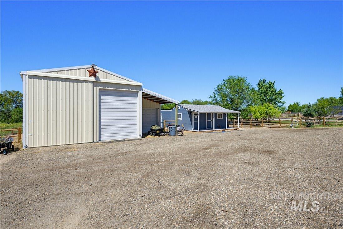 24623 Falcon Lane Caldwell, ID 83607 - Photo 36 of 40 Gravel lot featuring a metal building with a roll-up garage door, an attached lean-to structure, and a separate blue outbuilding with a covered porch