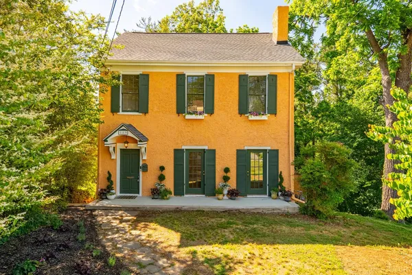 a view of a brick house with a yard plants and large tree