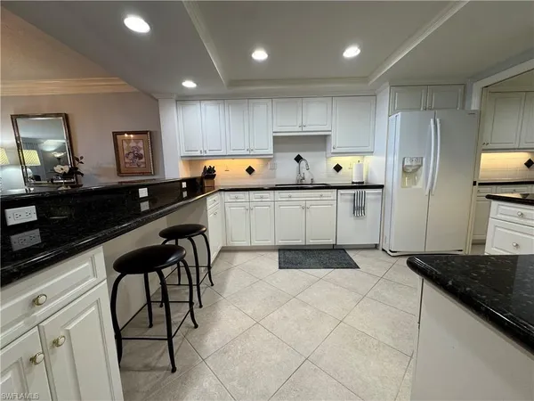 a kitchen with stainless steel appliances a sink a stove a refrigerator cabinets and chairs
