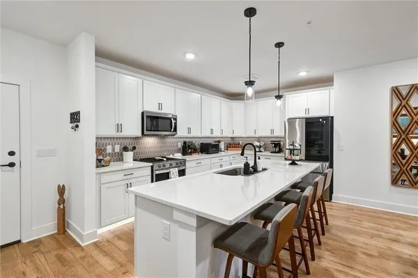 a kitchen with stainless steel appliances granite countertop a sink a stove a refrigerator and white cabinets with wooden floor