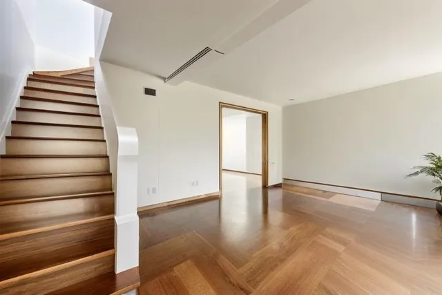 a view of an empty room with wooden floor and stairs