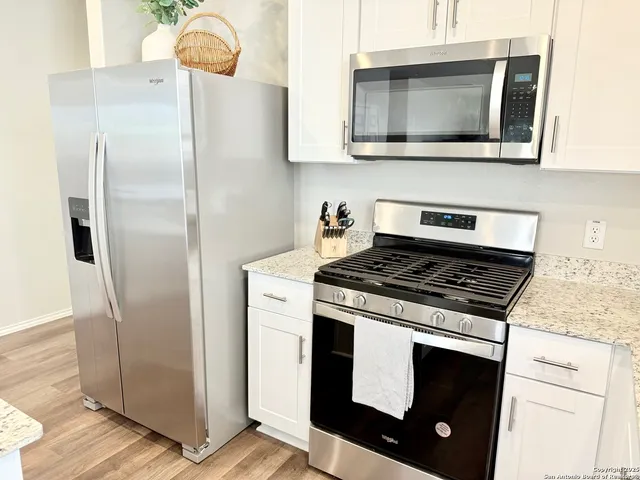 a kitchen with stainless steel appliances a stove top oven a sink a refrigerator white cabinets and wooden floor