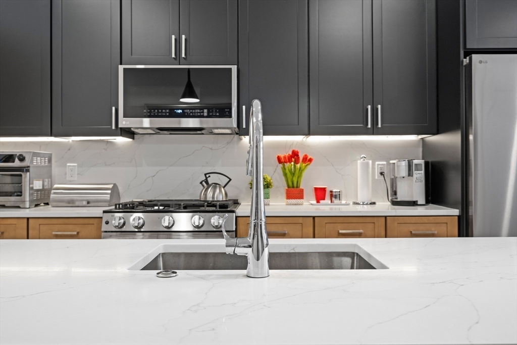 231 Everett Street, Unit 1 Boston, MA 02128 - Photo 13 of 39 a kitchen with kitchen island a sink and a stove with wooden floor