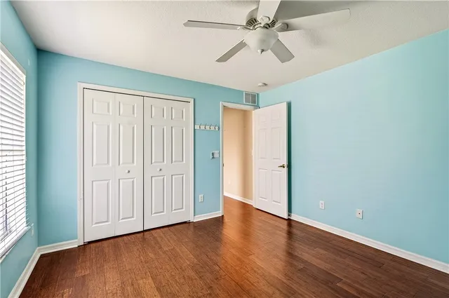 an empty room with wooden floor chandelier fan and windows
