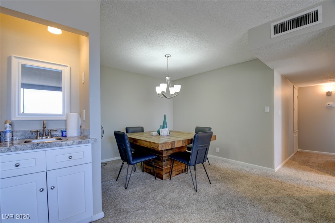 745 North Royal Crest Circle, Unit 127 Las Vegas, NV 89169 - Photo 17 of 26 Dining area featuring a chandelier, light carpet, a textured ceiling, and baseboards