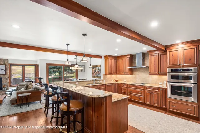 a kitchen with stainless steel appliances granite countertop a stove top oven a sink dishwasher a dining table and chairs with wooden floor