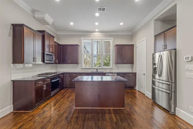 a kitchen with kitchen island granite countertop wooden floors stainless steel appliances a sink and a window