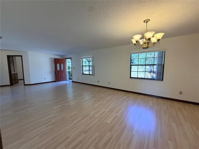 an empty room with wooden floor chandelier and windows