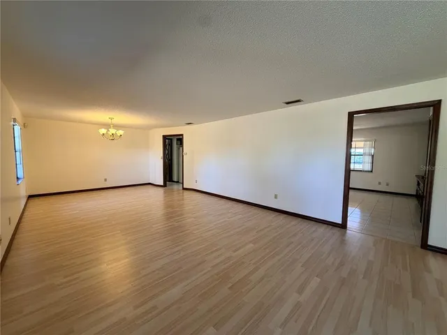 an empty room with wooden floor chandelier fan and windows