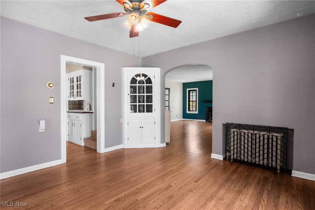 3677 Traver Road Shaker Heights, OH 44122 - Photo 10 of 35 Empty room featuring arched walkways, a ceiling fan, wood finished floors, baseboards, and a fireplace