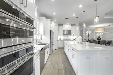 a kitchen with stainless steel appliances kitchen island granite countertop a stove top oven a sink a dining table and chairs with wooden floor