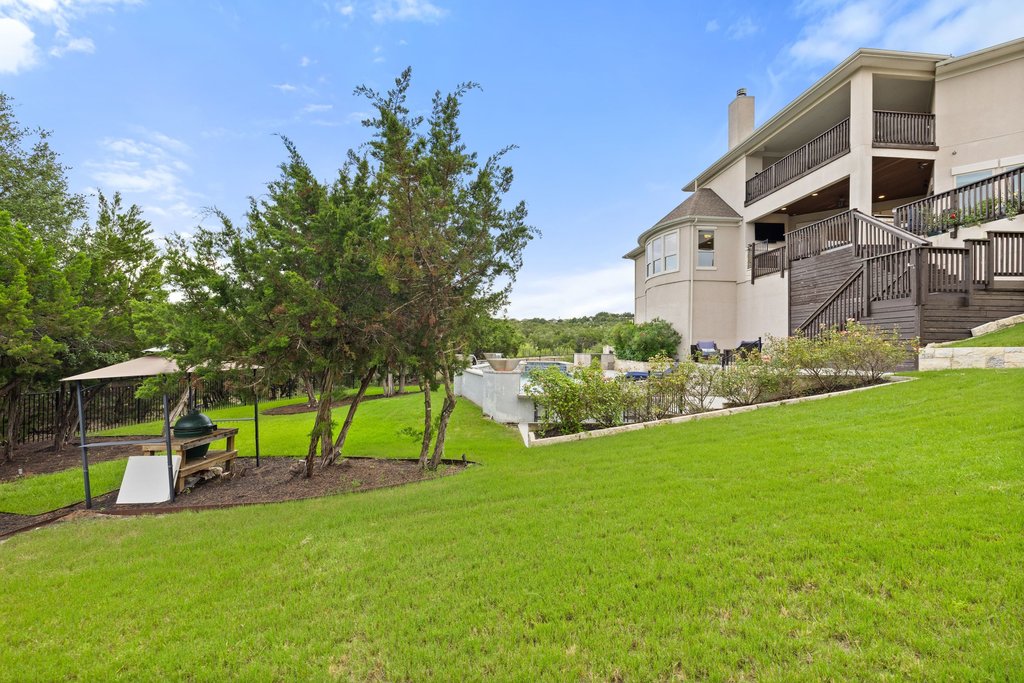 215 Lodestone Lane Austin, TX 78738 - Photo 39 of 40 A tiered backyard oasis with lush green grass, mature trees, and a spacious deck, perfect for outdoor living.