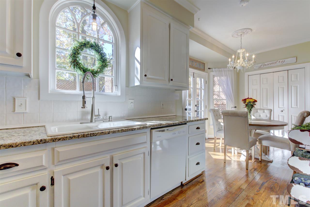 4417 Lancashire Drive Raleigh, NC 27613 - Photo 5 of 30 a kitchen with granite countertop white cabinets white appliances a large window and wooden floor