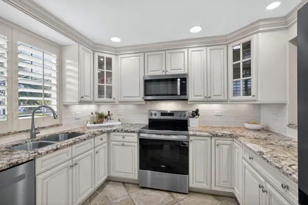 a kitchen with granite countertop white cabinets stainless steel appliances and a window