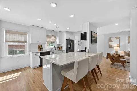 a large white kitchen with stainless steel appliances granite countertop a stove a sink a dining table and chairs