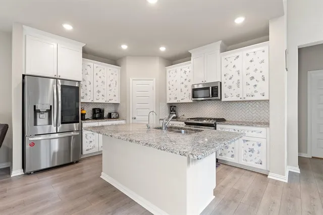 a kitchen with stainless steel appliances granite countertop a refrigerator a stove a sink and white cabinets with wooden floor