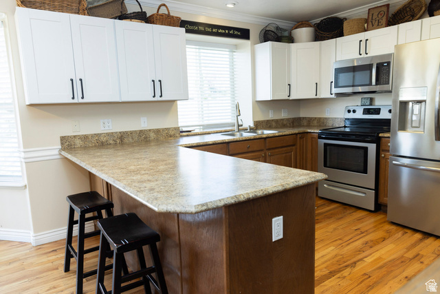 7532 North Castle Rock Road Eagle Mountain, UT 84005 - Photo 6 of 40 Kitchen featuring a peninsula, a kitchen bar, stainless steel appliances, light wood-style flooring, and crown molding