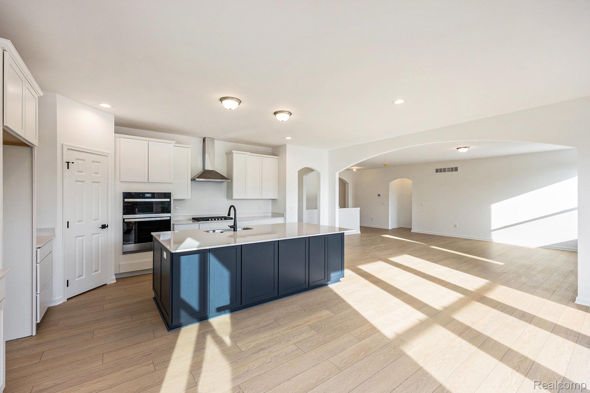 68788 Place Road New Haven, MI 48050 - Photo 7 of 29 Kitchen with white cabinetry, wall chimney exhaust hood, a kitchen island with sink, stainless steel double oven, and light wood-type flooring