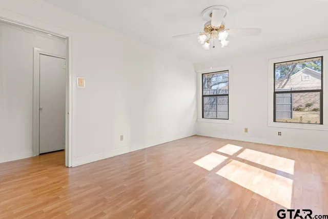 an empty room with wooden floor chandelier fan and windows
