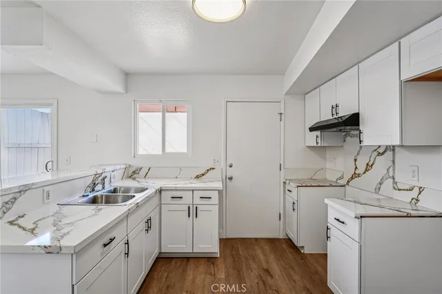 a kitchen with a sink dishwasher and white cabinets with wooden floor