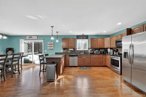 a kitchen with stainless steel appliances granite countertop a refrigerator a stove a sink a dining table and chairs with wooden floor