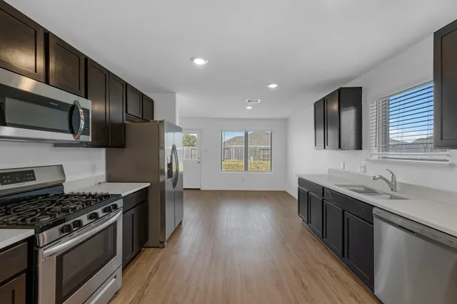 a kitchen with stainless steel appliances wooden cabinets granite counter tops a stove a sink and hard wood floors