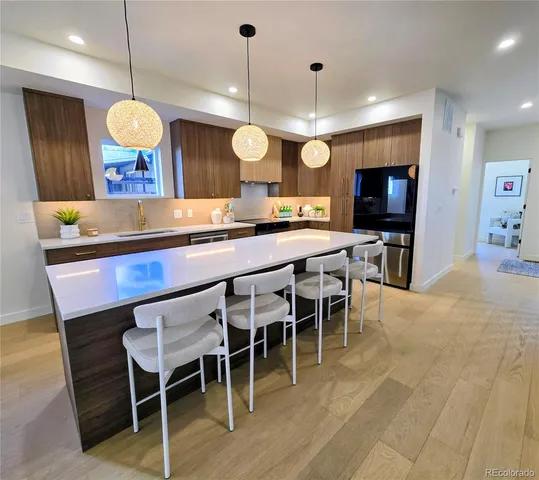 a kitchen with stainless steel appliances granite countertop a stove top oven a refrigerator a dining table and chairs with wooden floor