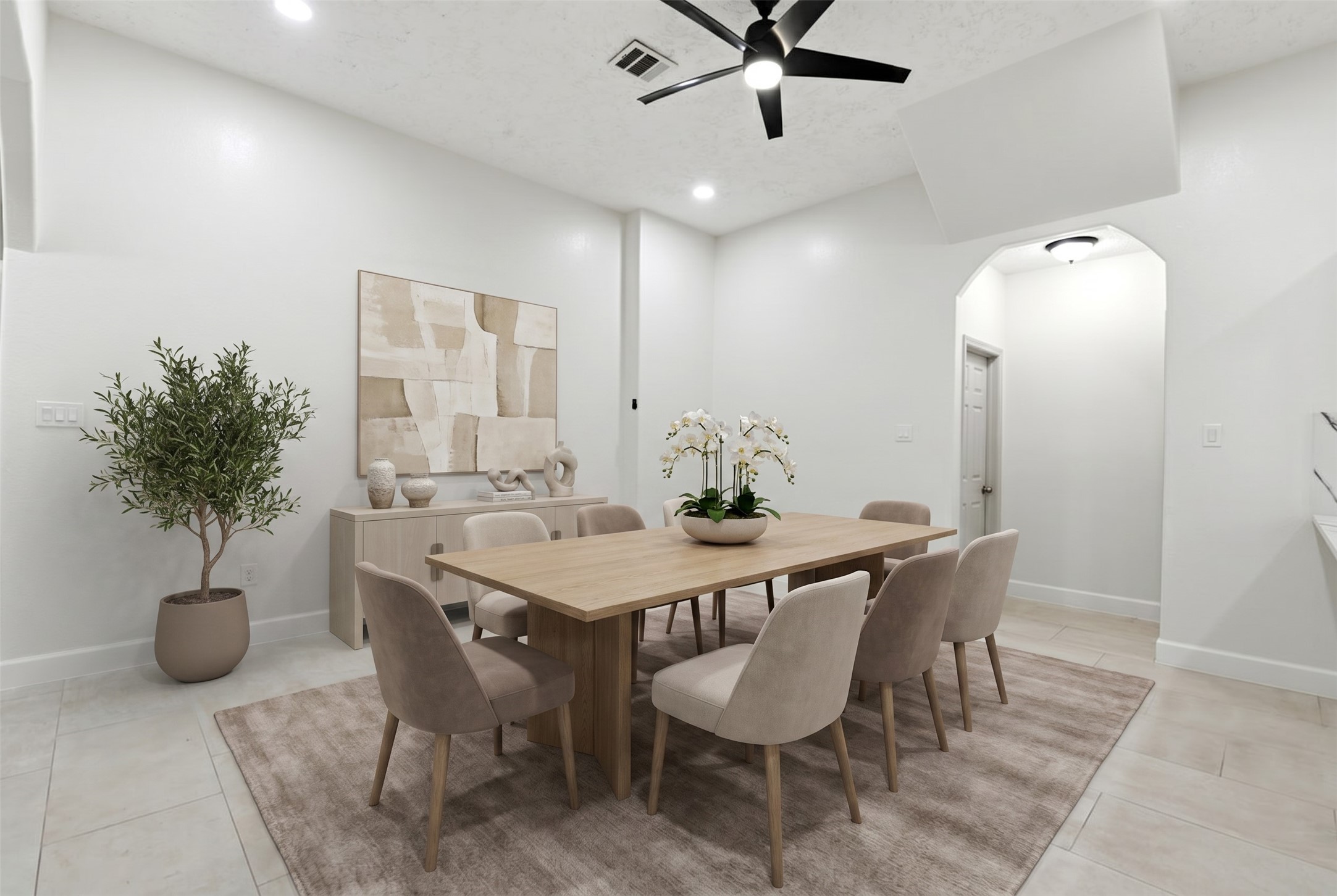 9403 Spaulding Street Houston, TX 77016 - Photo 13 of 50 This is a modern, open dining area featuring a large wooden table with eight upholstered chairs, neutral decor, and a ceiling fan. The space has a light and airy feel, enhanced by a large rug, potted plant, and elegant artwork on the wall.