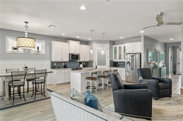 a living room with stainless steel appliances kitchen island granite countertop a dining table chairs and a refrigerator
