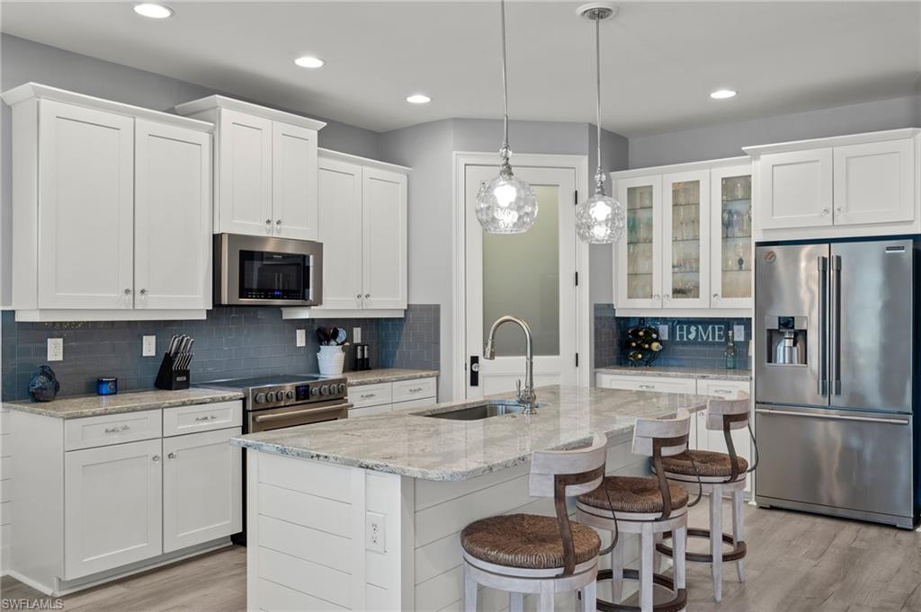 14651 Topsail Drive Naples, FL 34114 - Photo 7 of 37 a kitchen with a refrigerator a microwave a stove and white cabinets with wooden floor