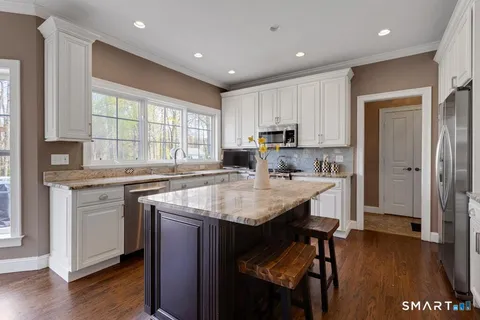 a kitchen with stainless steel appliances granite countertop a sink a stove a refrigerator and island with wooden floor