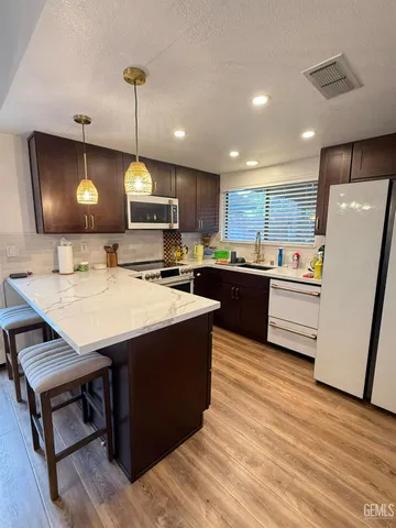 a kitchen with kitchen island a stove a refrigerator a sink a dining table and chairs with wooden floor