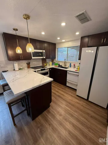 a kitchen with a refrigerator a stove top oven a sink dishwasher and a dining table with wooden floor