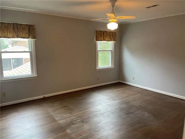 an empty room with wooden floor chandelier fan and windows