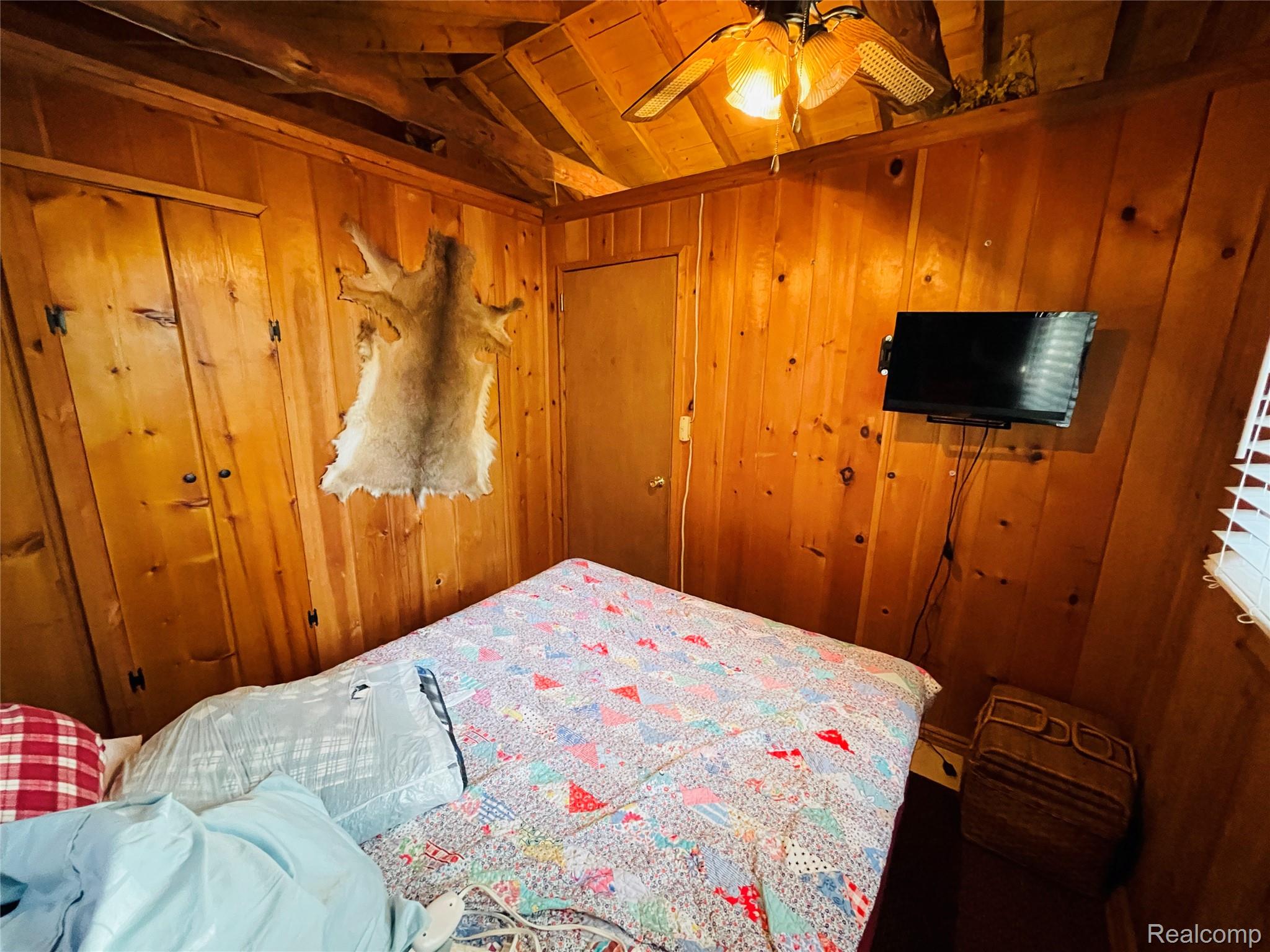 417 Ogemaw Road Rose City, MI 48654 - Photo 8 of 26 Wood-paneled walls and ceiling, ceiling-mounted fan with integrated lighting, wall-mounted television, and a built-in closet with double doors
