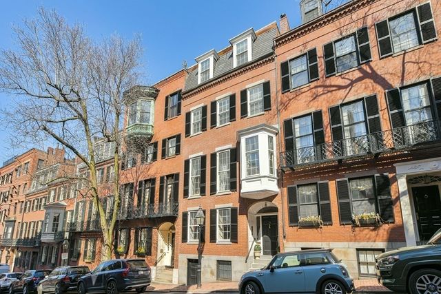 a front view of a building with lot of cars and trees