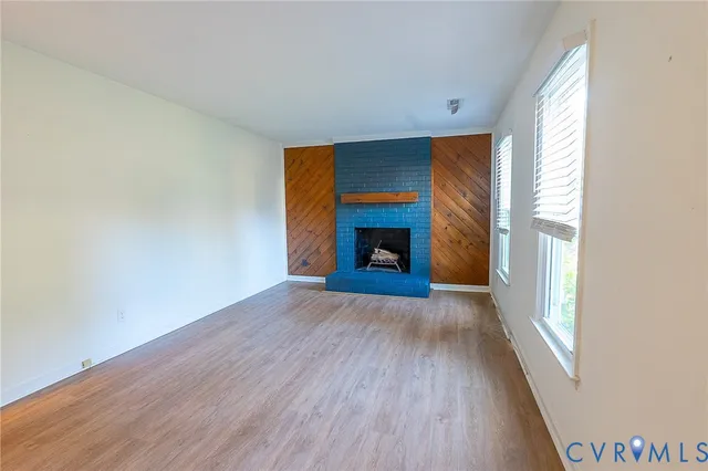 a view of an empty room with wooden floor fireplace and a window