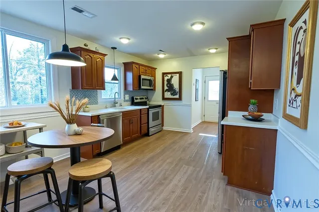 a kitchen with stainless steel appliances kitchen island granite countertop a refrigerator a stove a sink a dining table and chairs with wooden floor