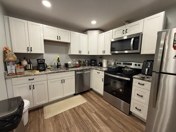 a kitchen with stainless steel appliances white cabinets a sink a stove a refrigerator and microwave with wooden floor