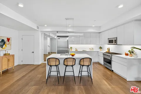 a kitchen with stainless steel appliances granite countertop a stove top oven a sink dishwasher and white cabinets with wooden floor