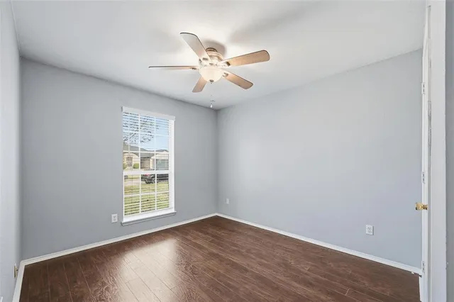 an empty room with wooden floor fan and windows