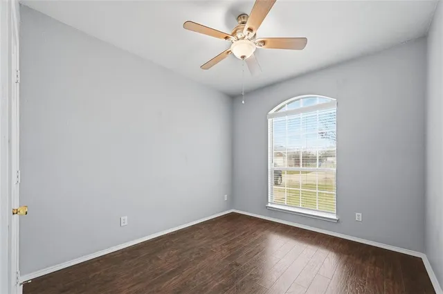 an empty room with wooden floor chandelier fan and windows