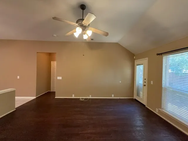 an empty room with wooden floor fan and windows