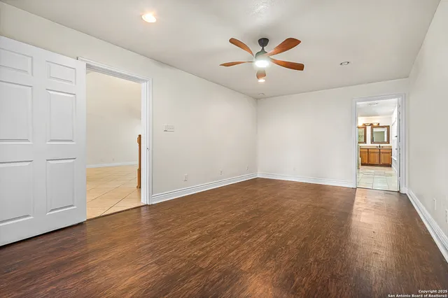an empty room with wooden floor chandelier fan and windows