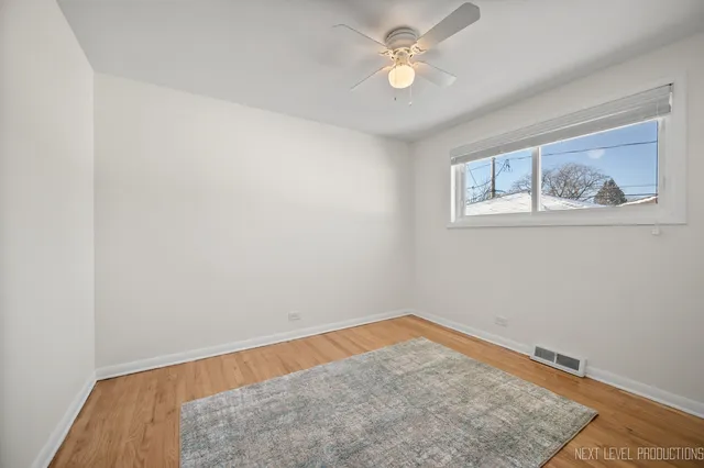 an empty room with a chandelier fan and wooden floor