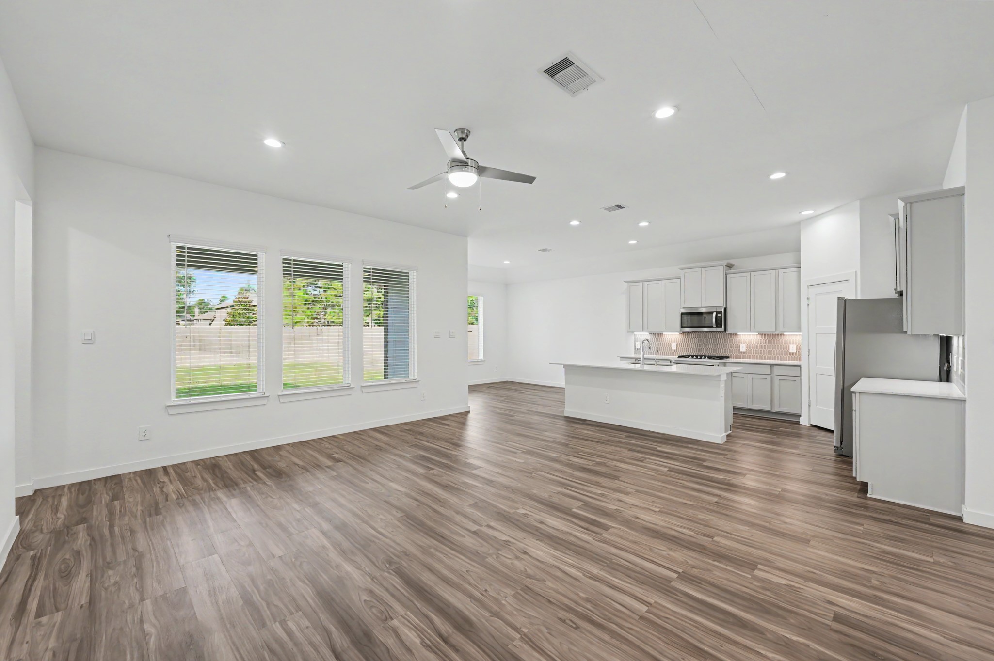 14162 Primrose Ridge Lane Conroe, TX 77384 - Photo 13 of 48 Spacious open-concept living area with sleek wood flooring, abundant natural light from large windows, and a modern kitchen featuring stainless steel appliances and a central island.